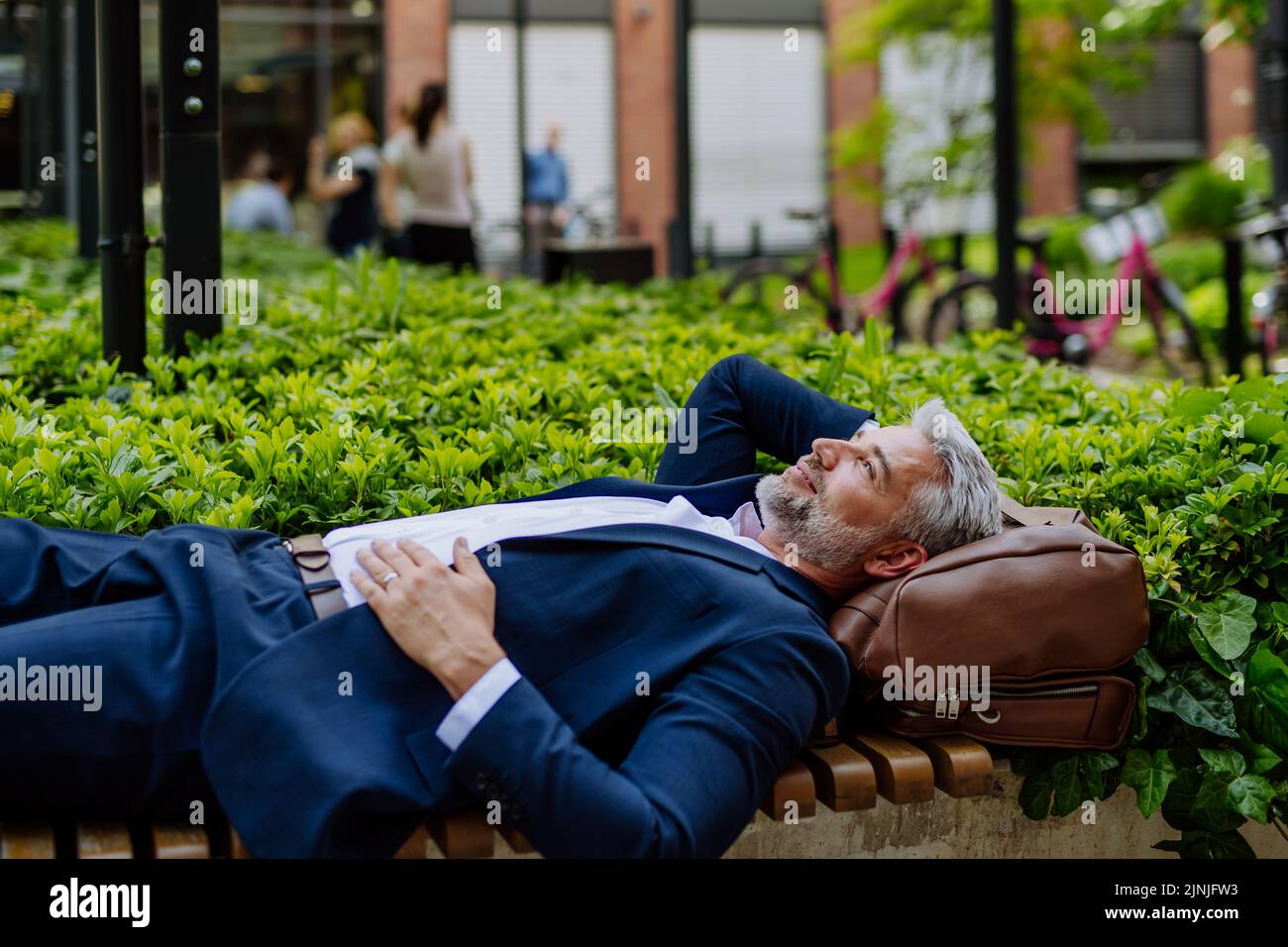 Uomo d'affari maturo che si rilassa su panchina nel parco cittadino durante la pausa al lavoro, concetto di equilibrio vita-lavoro. Foto Stock