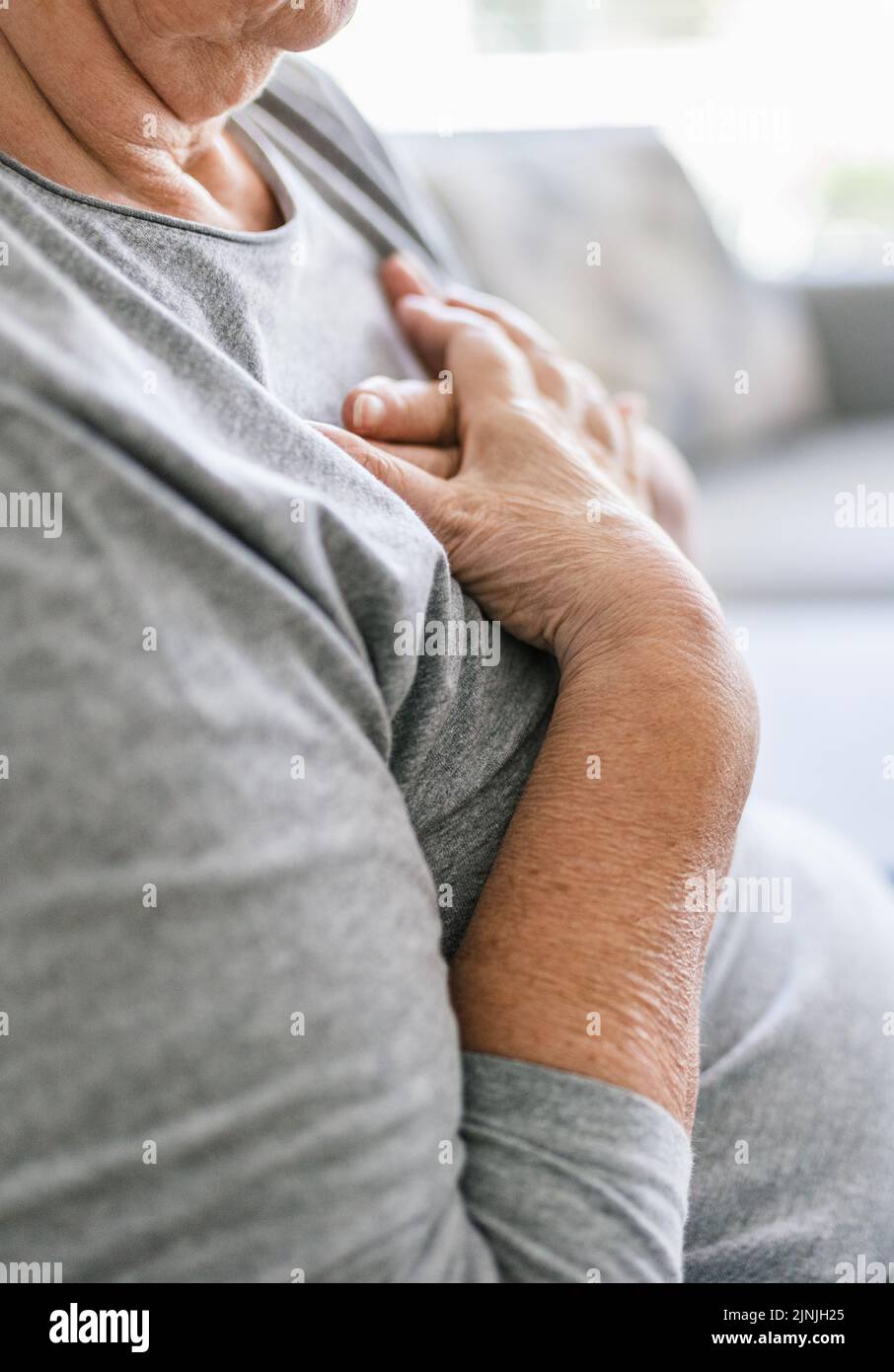Donna anziana a casa con dolore al cuore che le tiene il petto Foto Stock
