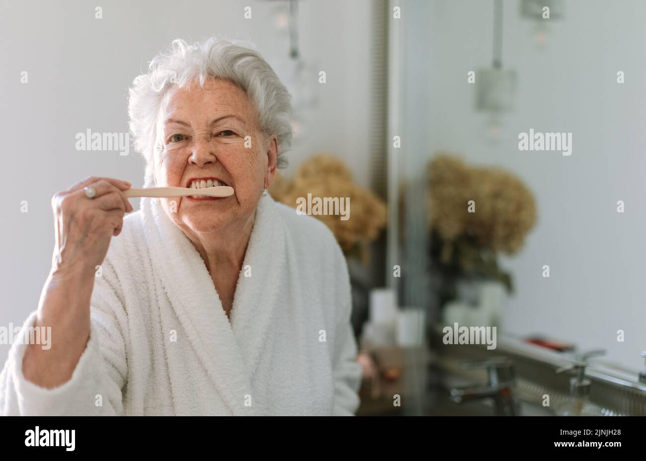 Donna anziana che pulisce i denti con spazzola di legno in bagno, stile di vita sostenibile. Foto Stock
