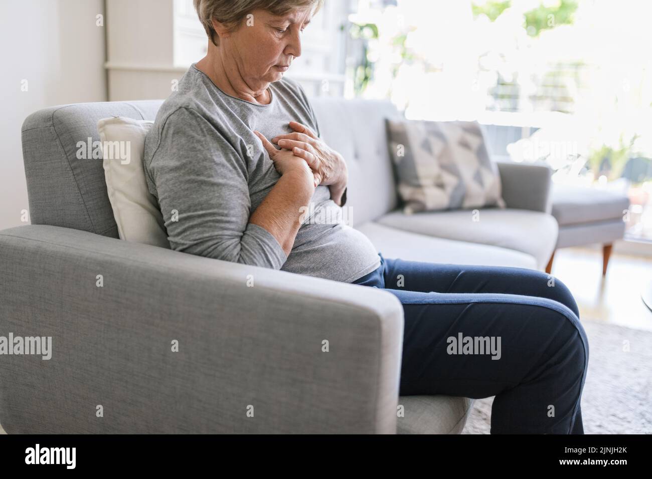 Donna anziana a casa con dolore al cuore che le tiene il petto Foto Stock