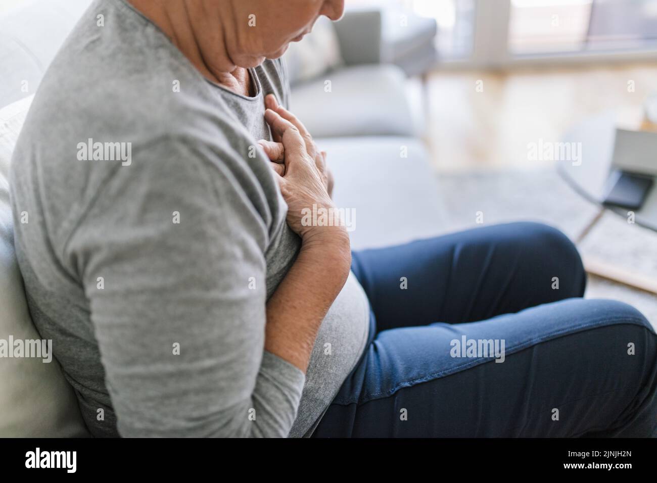 Donna anziana a casa con dolore al cuore che le tiene il petto Foto Stock