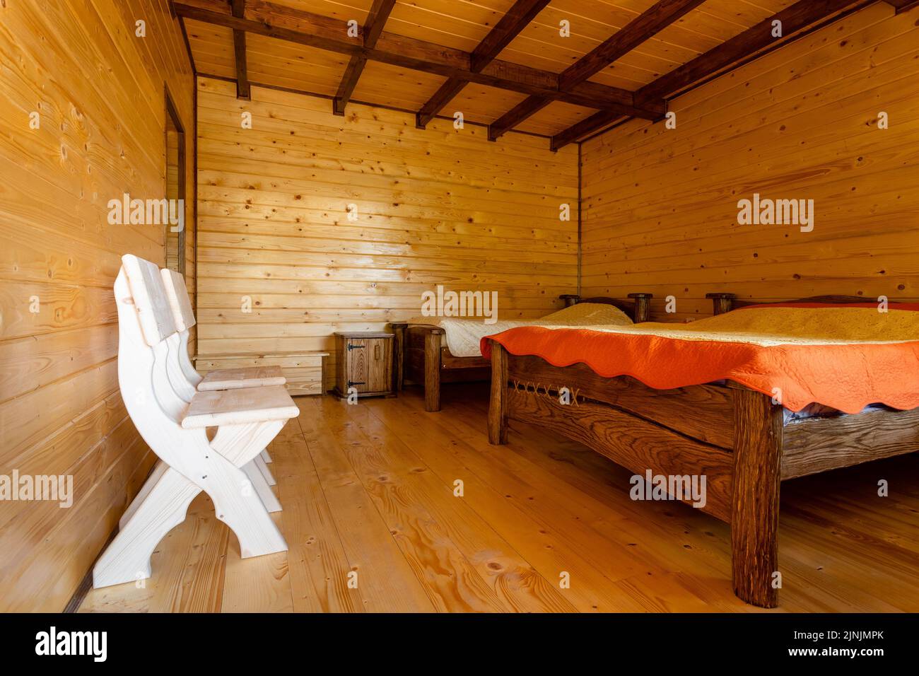 Piccola camera da letto con due letti in legno, sedie e comodini in un moderno cottage con pareti in legno. Mobili fatti a mano. Foto Stock