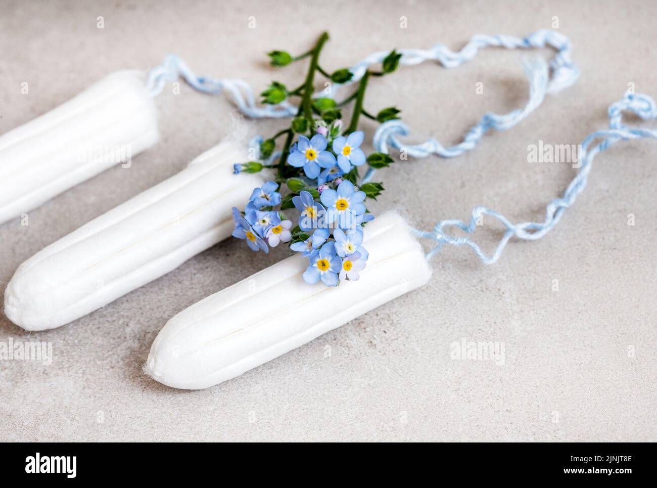 igiene femminile, tamponi e fiori dimenticare-me-non sul grigio Foto Stock