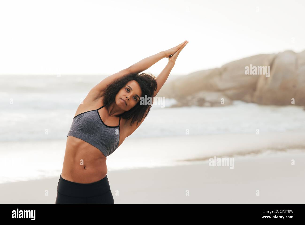 Donna che stretching il suo corpo su una spiaggia. Giovane donna che si scalda prima degli esercizi di yoga. Foto Stock
