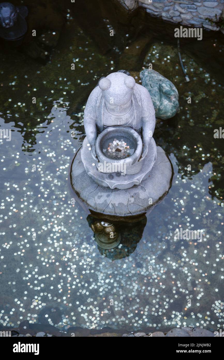 Una foto verticale di una fontana di desiderio con monete al Tempio di Yakcheonsa sull'isola di Jeju, Corea del Sud Foto Stock