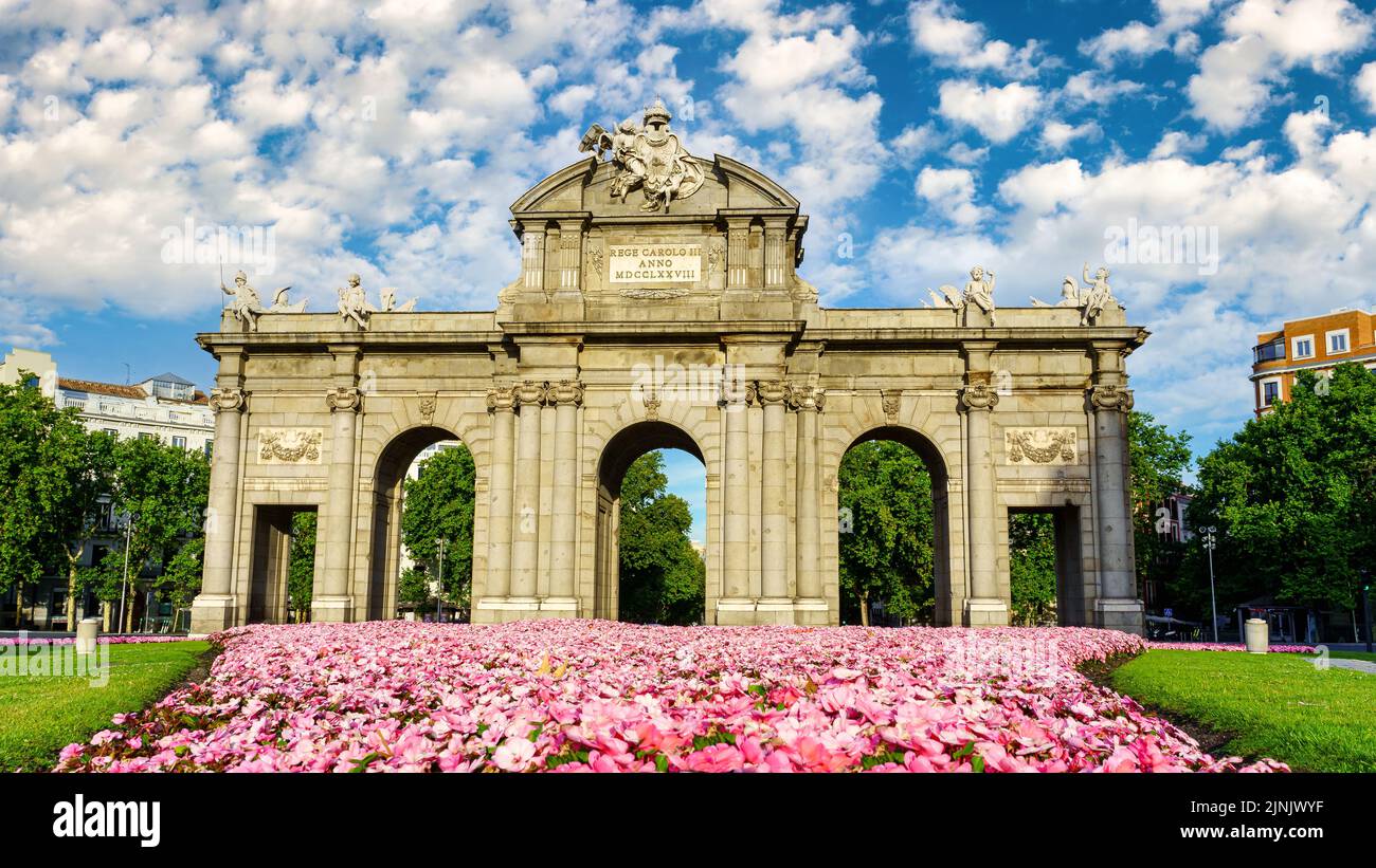 Puerta de Alcala de Madrid in fiori sul terreno e giorno di sole con nuvole bianche. Foto Stock