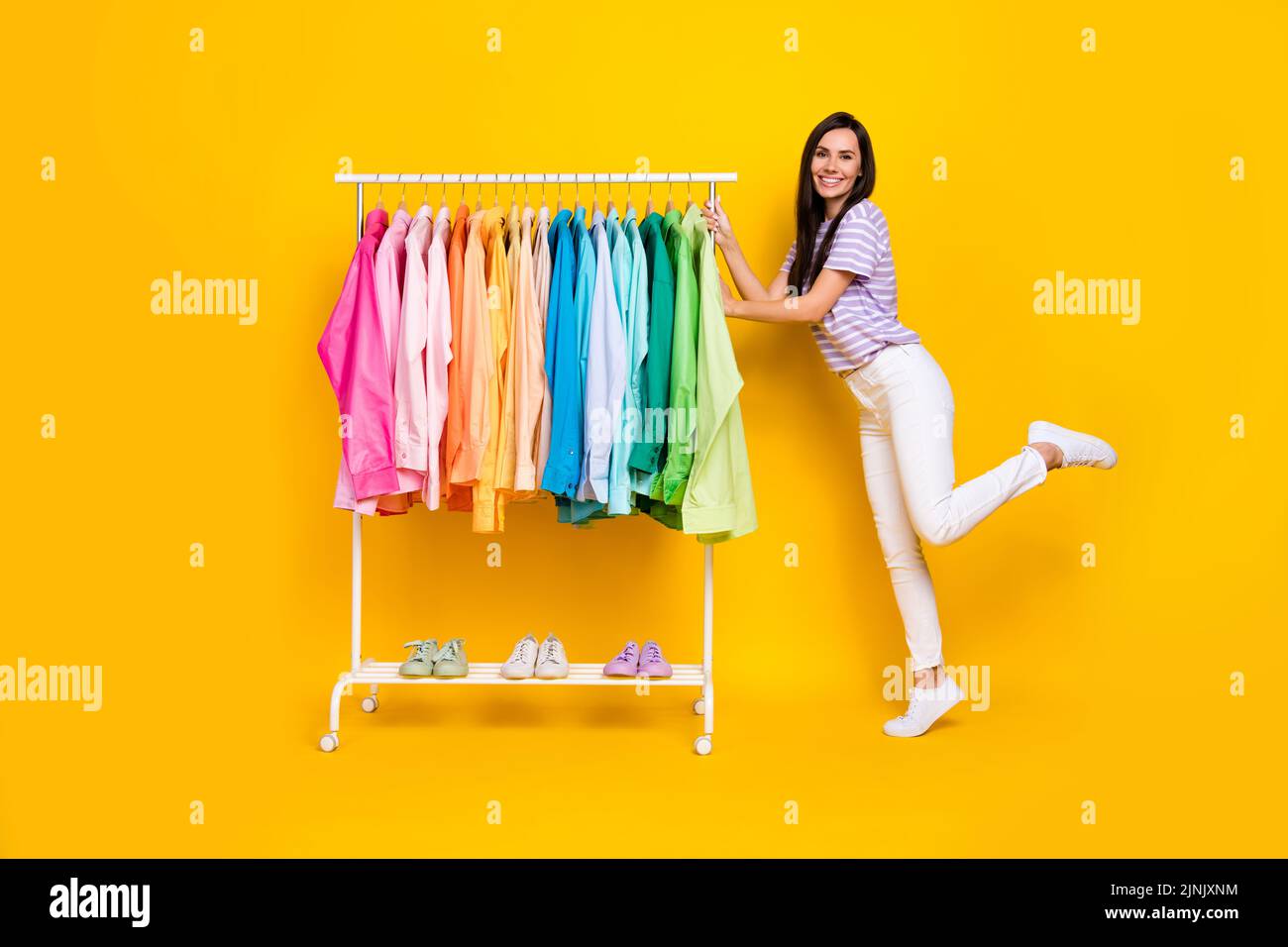 Foto a grandezza naturale di una giovane e attraente assistente che mostra l'assortimento della sua boutique isolata su sfondo di colore giallo Foto Stock