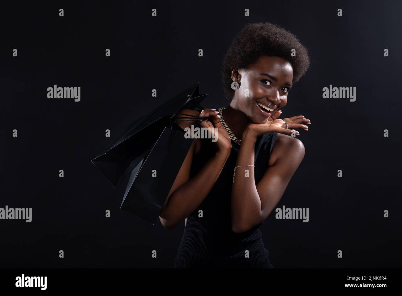 Donna afroamericana con acconciatura afro contiene borse nere per la spesa. Concetto di Black Friday. Foto Stock