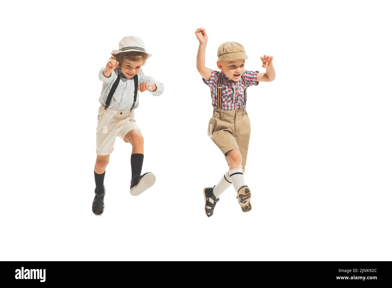 Due ragazzi dell'età prescolare, eleganti ragazzi che indossano abiti retrò che corrono isolati su sfondo bianco. Concetto di infanzia, stile di moda d'estate vintage Foto Stock