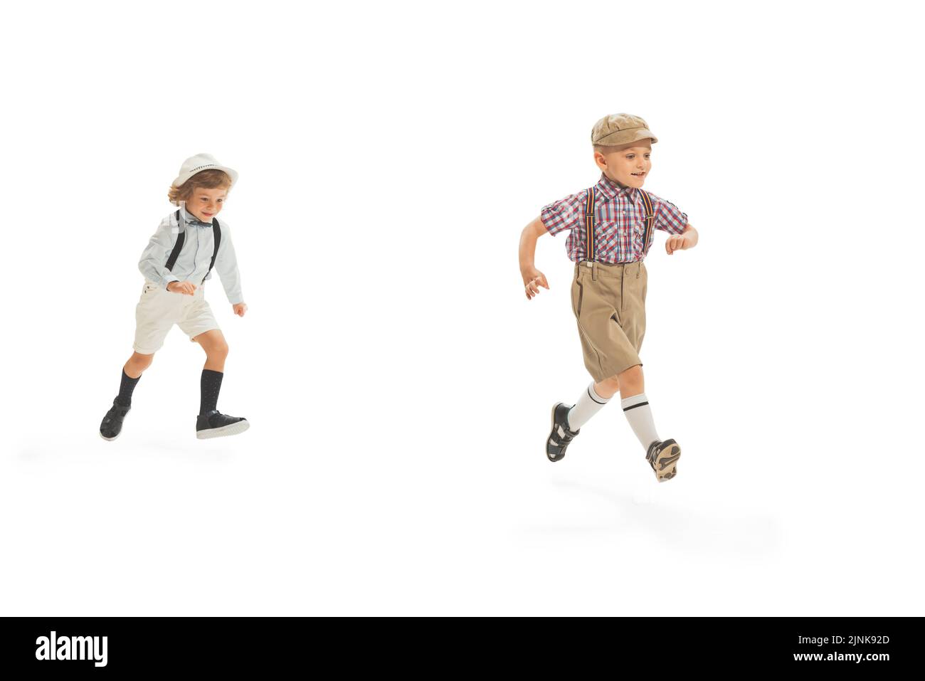 Due ragazzi dell'età prescolare, eleganti ragazzi che indossano abiti retrò che corrono isolati su sfondo bianco. Concetto di infanzia, stile di moda d'estate vintage Foto Stock