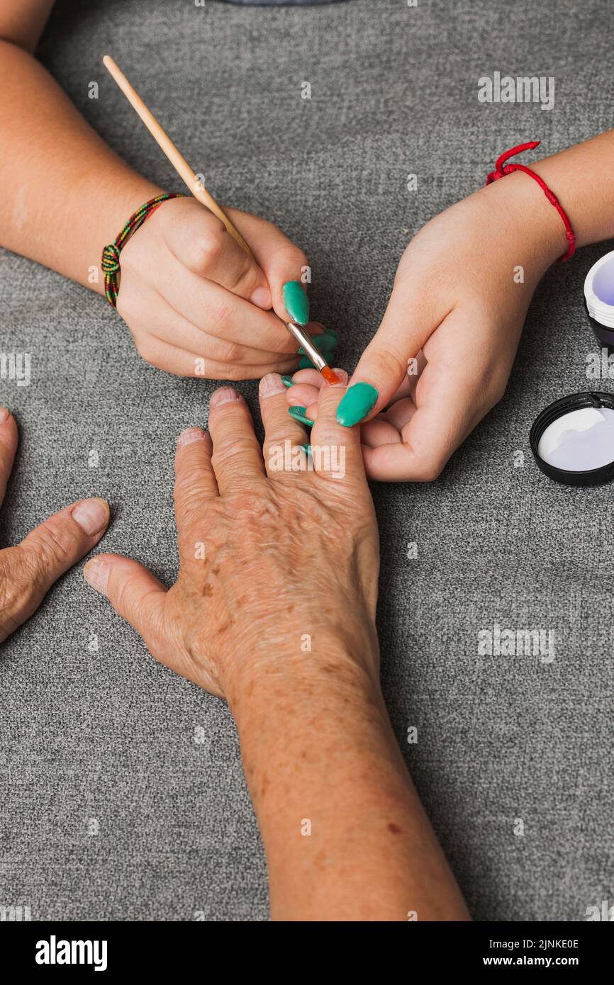 Primo piano delle mani di due donne irriconoscibili, una giovane e una anziana, che hanno una manicure. La giovane donna sta applicando il gel con un pennello sul più anziano Foto Stock