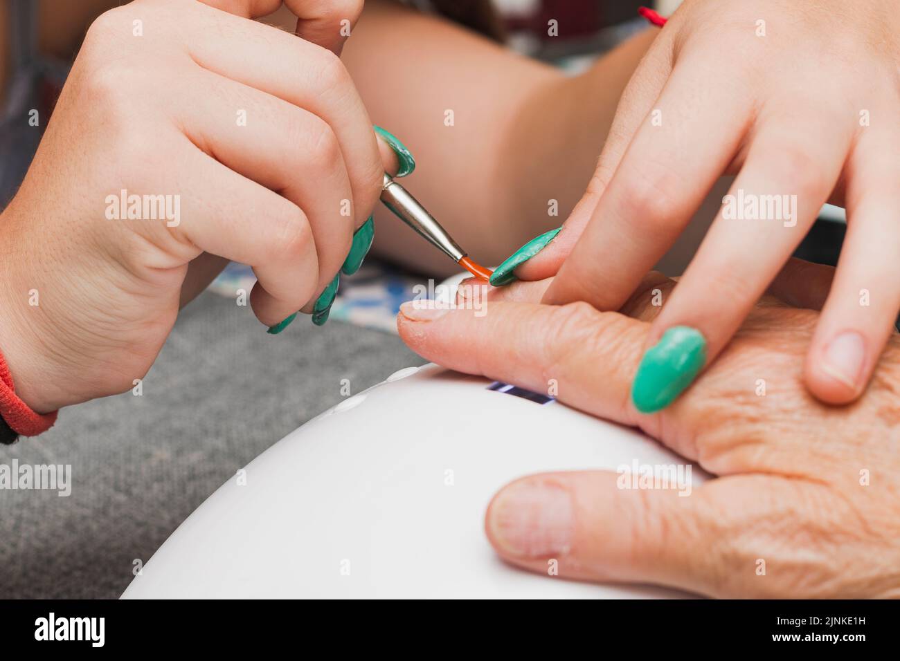 Primo piano delle mani di due donne irriconoscibili, una giovane e una anziana, che hanno una manicure. La giovane donna sta applicando il gel con un pennello con un oran Foto Stock