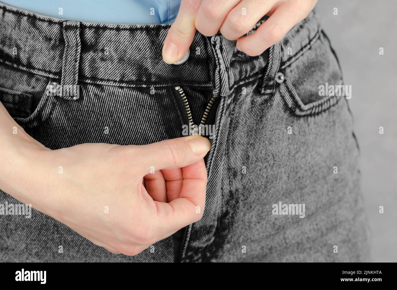 Le mani delle donne allacciano o dischiudono il mosca sui jeans, primo piano Foto Stock