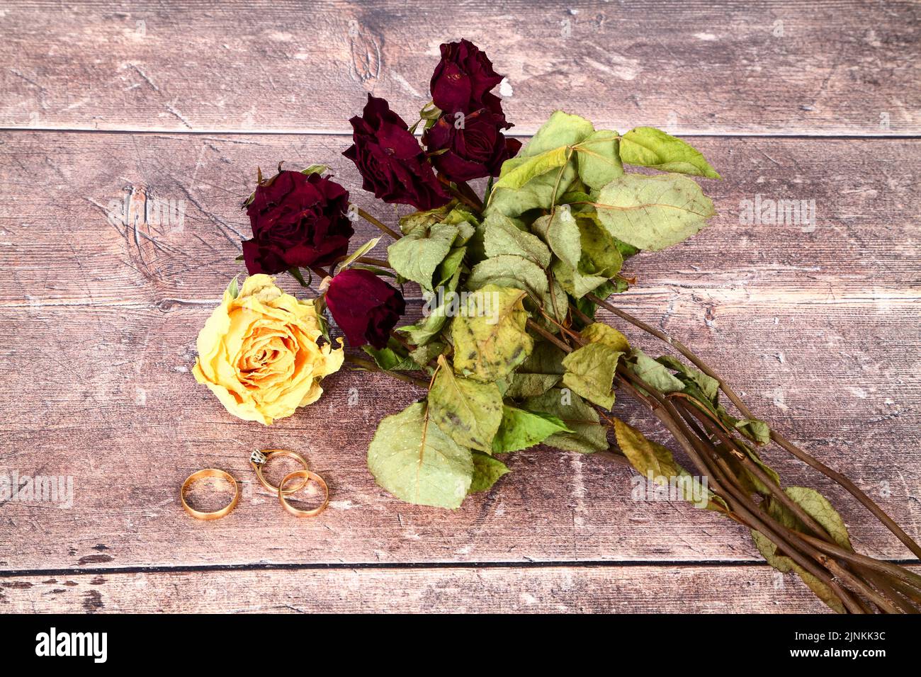Fiori di rosa appassiti morti e matrimonio e un anello di fidanzamento su un tavolo in legno Foto Stock