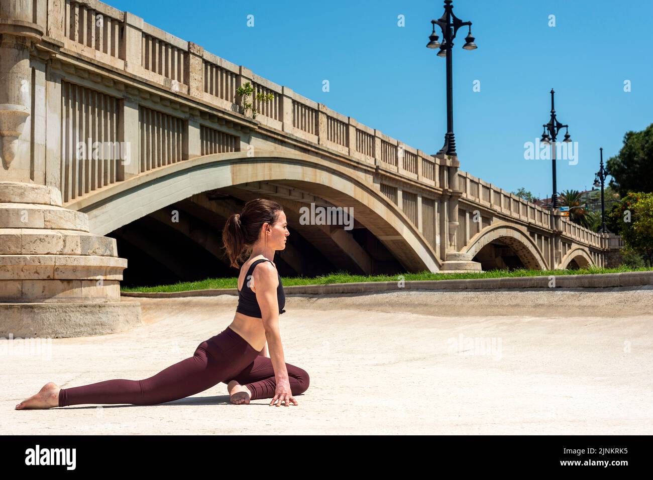 Donna sportiva in forma che fa yoga all'aperto da un ponte al sole. Foto Stock