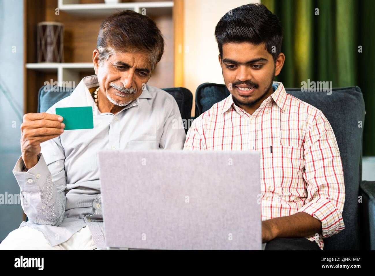 Figlio che effettua il pagamento in linea della fattura per lo shopping sul laptop con l'aiuto di padre che usa la carta di credito nel paese - concetto di e commercio, transazione sicura Foto Stock