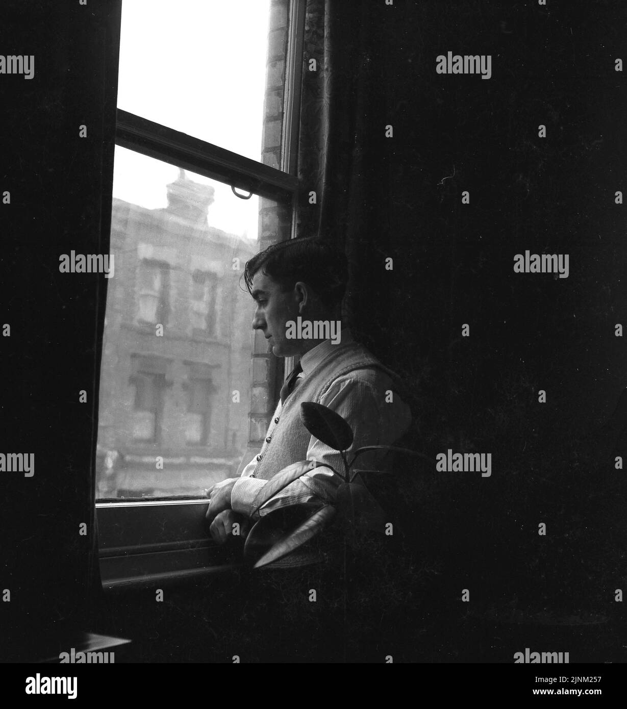 1950s, storico, all'interno di una casa, un uomo in piedi accanto a una finestra, guardando fuori sulla strada sotto, Inghilterra, Regno Unito. Foto Stock