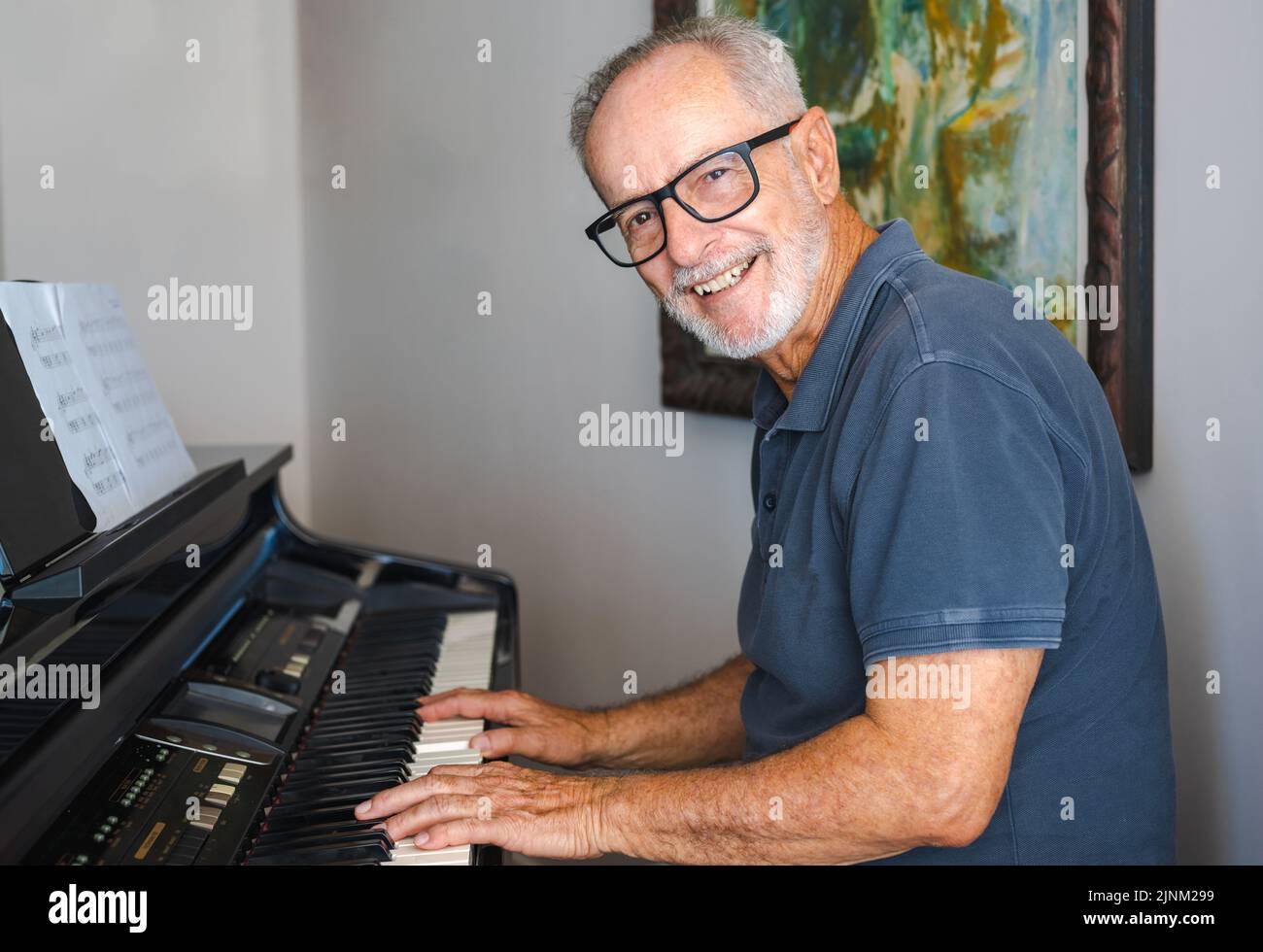 Uomo che pratica a suonare il pianoforte nel soggiorno della sua casa dopo il ritiro dal lavoro. Foto Stock