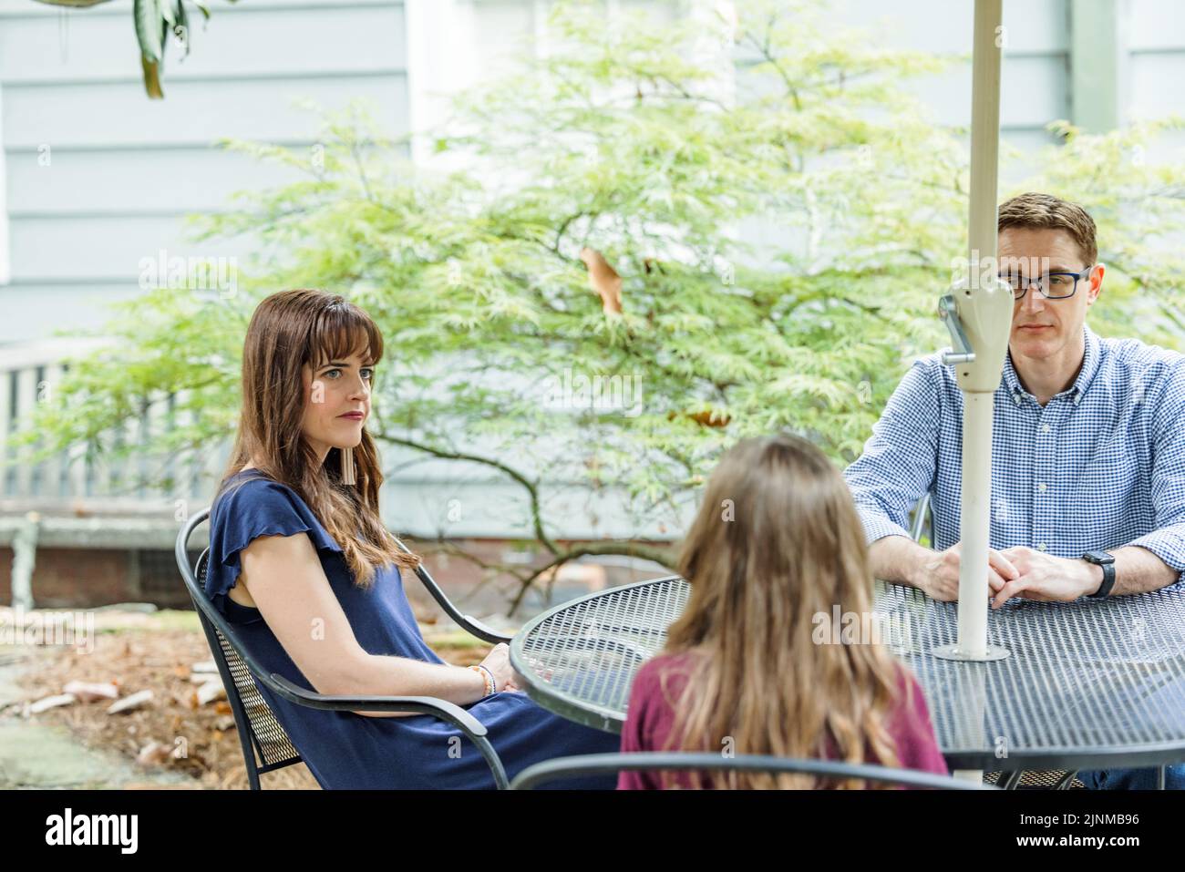 Una famiglia di una madre e di un padre e due figlie seduti al tavolo del patio con un ombrello che parla della loro giornata. Foto Stock