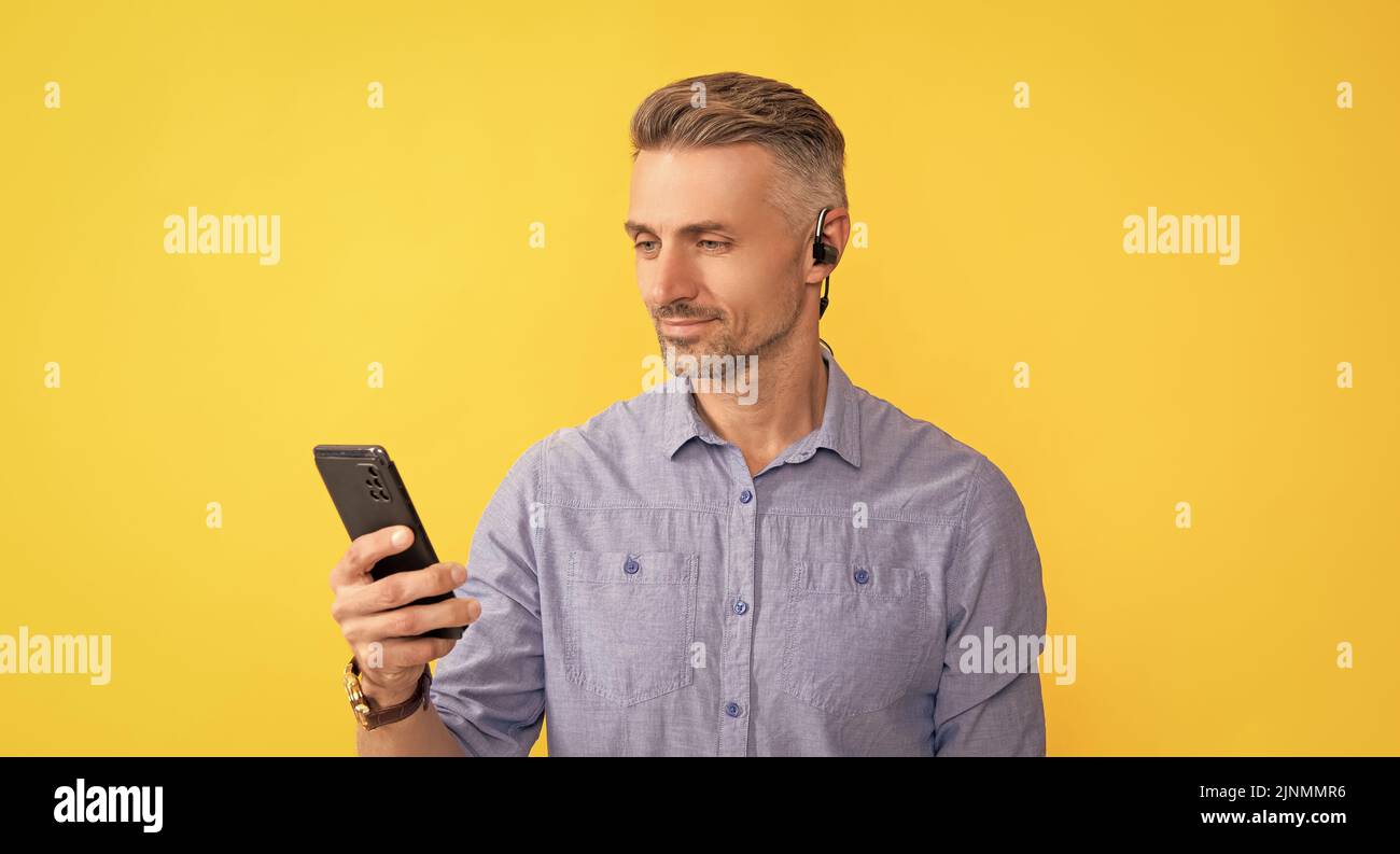 uomo sorridente che usa il telefono in cuffie su sfondo giallo, comunicazione Foto Stock