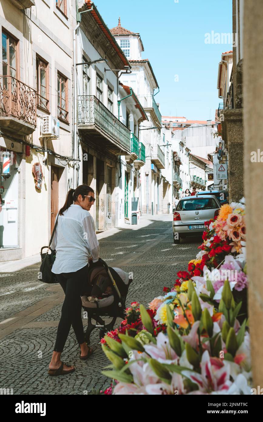 Vila Real, Portogallo - 2021, Settembre 15th - Donna che cammina con un bambino in una strada stretta con fiori a Vila Real Foto Stock