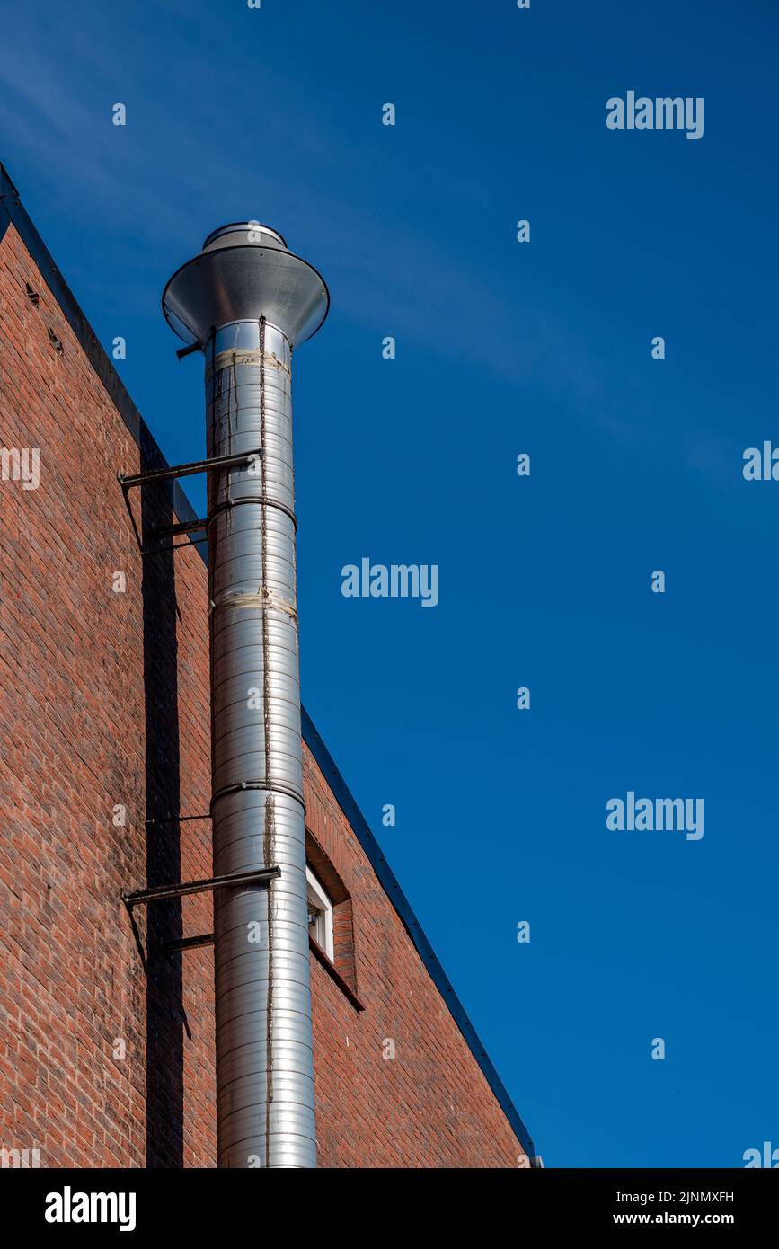 un tubo di scarico color argento su una parete della casa di fronte a un cielo blu Foto Stock
