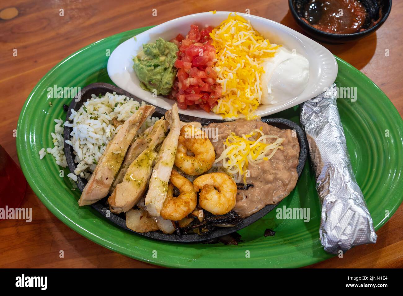 fajitas di pollo e gamberetti con fagioli e riso fritti e tortilla avvolta in un piatto verde in un ristorante Foto Stock