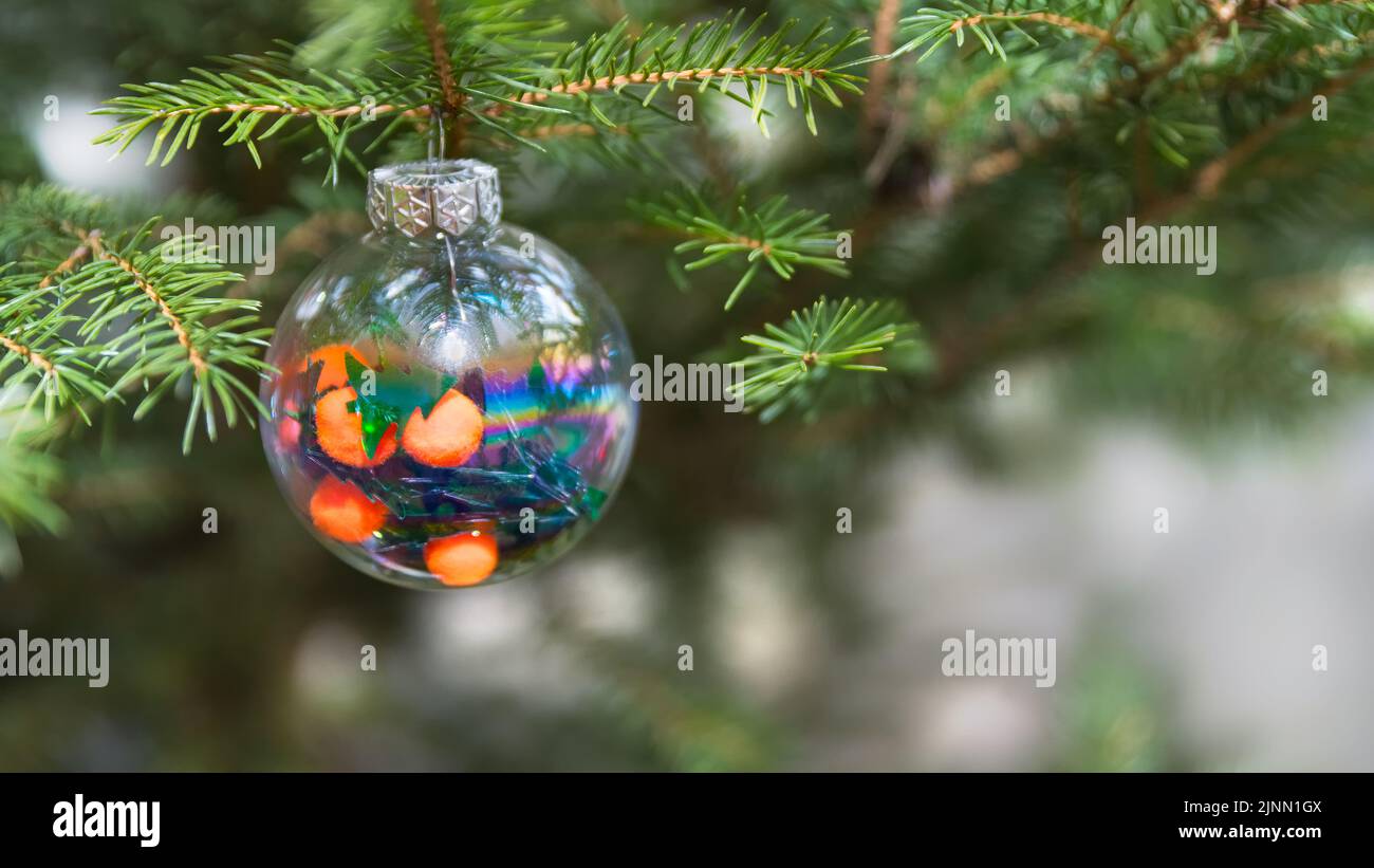 Albero di Natale verde con bella decorazione rotonda in vetro su uno sfondo bianco sfocato. Primo piano di ornamento natalizio appeso ad un ramo di abete naturale. Foto Stock