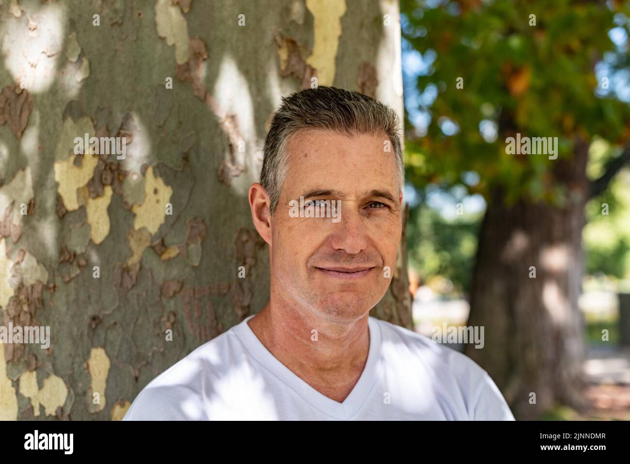 Un bell'uomo che si appoggia su un albero e guarda la telecamera Foto Stock