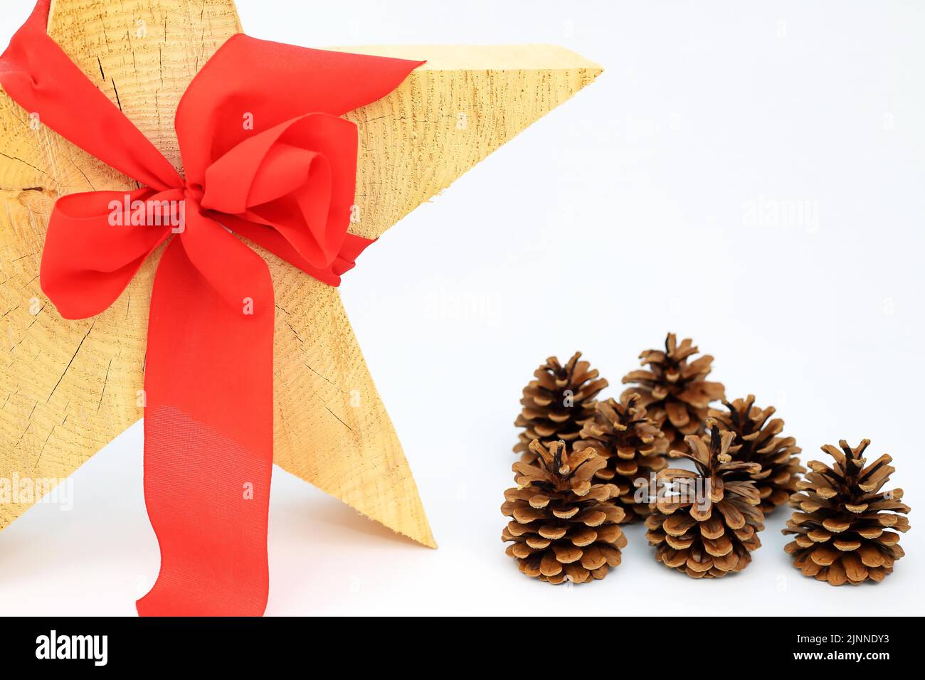 Stella di legno di Natale con arco rosso su fondo bianco, cono di pino o cono di pino sul lato Foto Stock