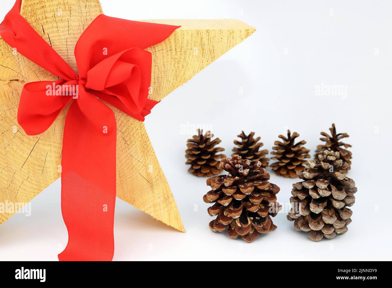 Stella di legno di Natale con arco rosso su fondo bianco, cono di pino o cono di pino sul lato Foto Stock