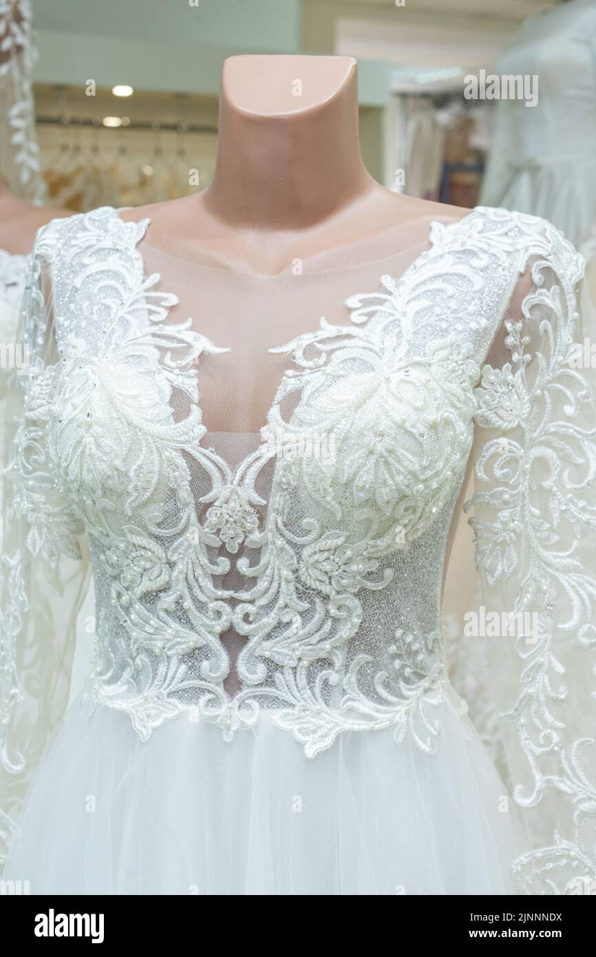 Un bel vestito da sposa bianco su un manichino. Primo piano di un abito contro altri abiti da sposa in un negozio di nozze. Foto Stock