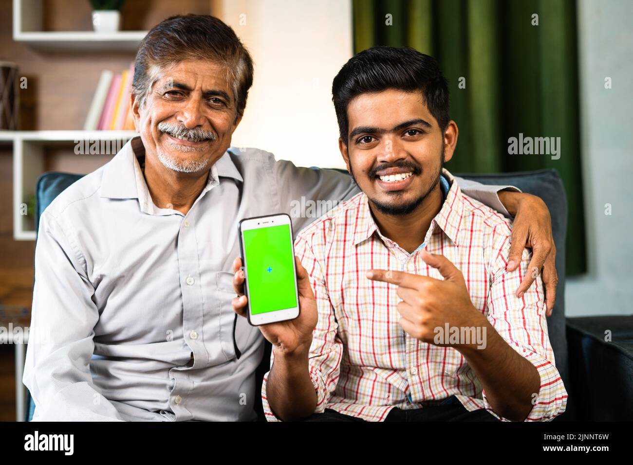 Concentratevi su figlio, nonno felice e nipote che mostrano il telefono cellulare con schermo verde puntando il dito mentre guardate la fotocamera a casa - concetto di app Foto Stock
