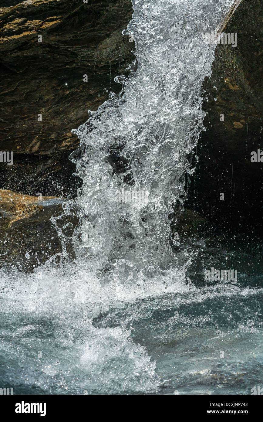 Getto d'acqua che cade da un torrente di montagna davanti ad una roccia. Con un'esposizione molto breve, l'acqua spruzzata appare come una colonna d'acqua congelata. Foto Stock