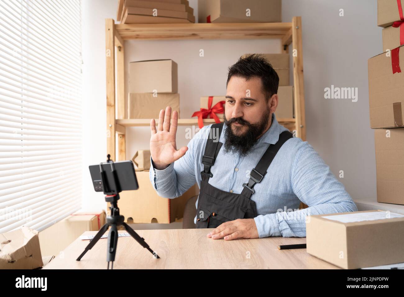 Un giovane uomo indiano che lavora con lo smartphone presso il negozio, consulente del negozio online che saluta la fotocamera dello smartphone. PMI, shopping online Foto Stock
