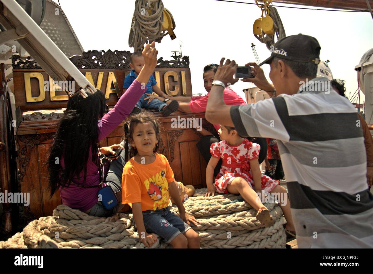 Un uomo sta scattando foto dei suoi parenti dei bambini in uno sfondo del cartello di KRI Dewaruci (Dewa Ruci), una nave alta indonesiana, mentre la goletta di tipo barquentino è aperta ai visitatori pubblici al porto di Kolinlamil (porto della Marina) a Tanjung Priok, nel nord di Giacarta, in Indonesia. Foto Stock