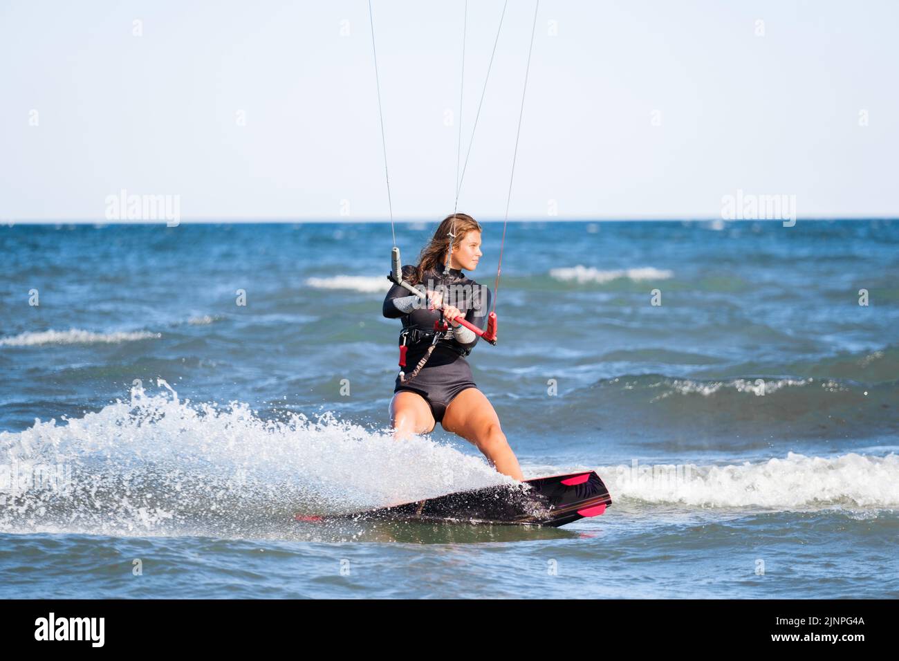 Kite surf ragazza in costume da bagno con aquilone nel cielo cavalca le onde con spruzzi d'acqua. Sport acquatici, donna sportiva, concetto d'azione e sport duri Foto Stock