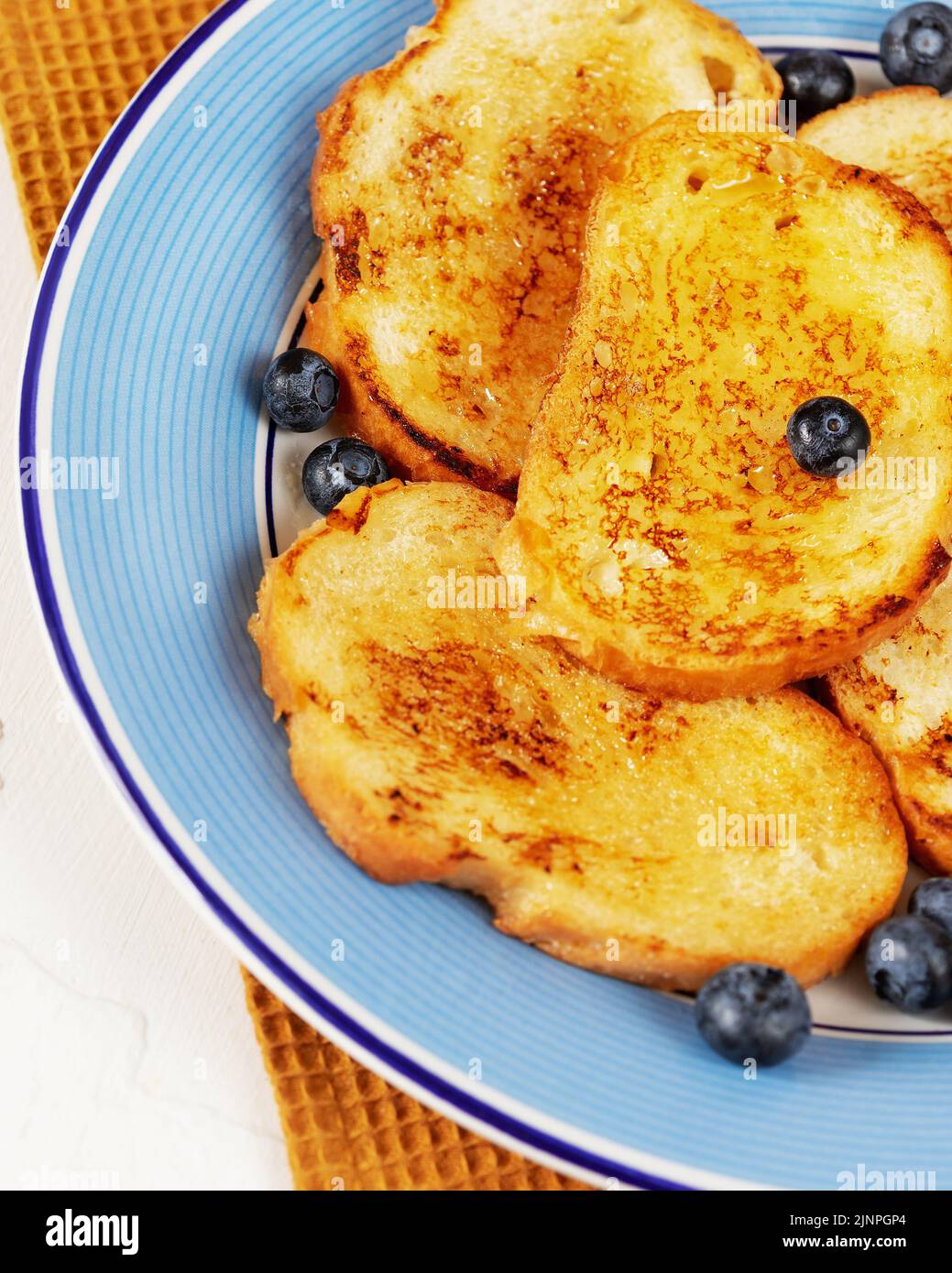 Dolci toast francesi con miele e mirtilli su un piatto blu su fondo bianco. Pane tostato per colazione. Dolce tradizionale di pane Foto Stock