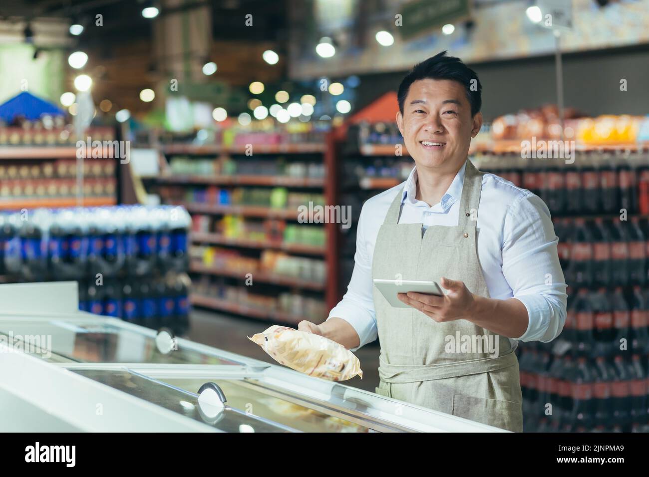 Ritratto del responsabile asiatico del negozio, uomo con tablet che controlla la data di scadenza dei prodotti, il venditore sorridendo e guardando la macchina fotografica vicino al frigorifero in supermercato Foto Stock