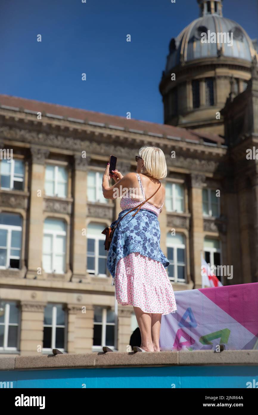 BIRMINGHAM, REGNO UNITO - 8 AGOSTO 2022. Una donna anziana che usa un telefono cellulare per scattare fotografie mentre è in vacanza in un ambiente cittadino Foto Stock
