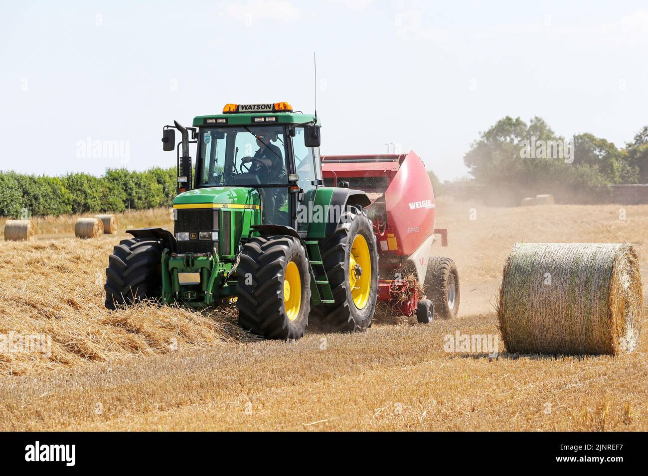 Il contadino locale guida il trattore e l'imballatrice John Dere per raccogliere e imballare il grano da tagliare per immagazzinare l'animale da lettiera e l'uso agricolo generale in inverno. N Foto Stock