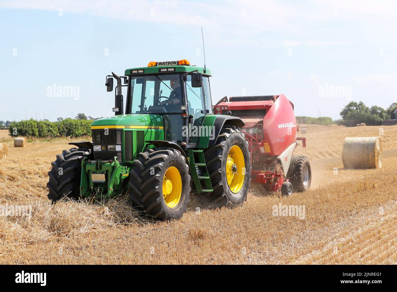 Il contadino locale guida il trattore e l'imballatrice John Dere per raccogliere e imballare il grano da tagliare per immagazzinare l'animale da lettiera e l'uso agricolo generale in inverno. N Foto Stock