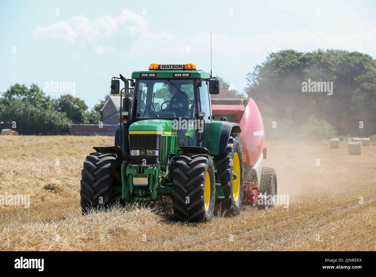 Il contadino locale guida il trattore e l'imballatrice John Dere per raccogliere e imballare il grano da tagliare per immagazzinare l'animale da lettiera e l'uso agricolo generale in inverno. N Foto Stock