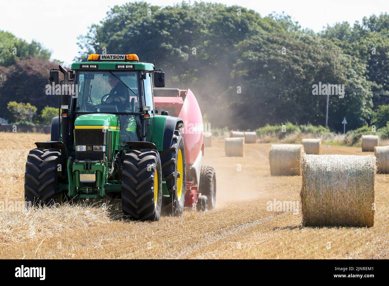 Il contadino locale guida il trattore e l'imballatrice John Dere per raccogliere e imballare il grano da tagliare per immagazzinare l'animale da lettiera e l'uso agricolo generale in inverno. N Foto Stock