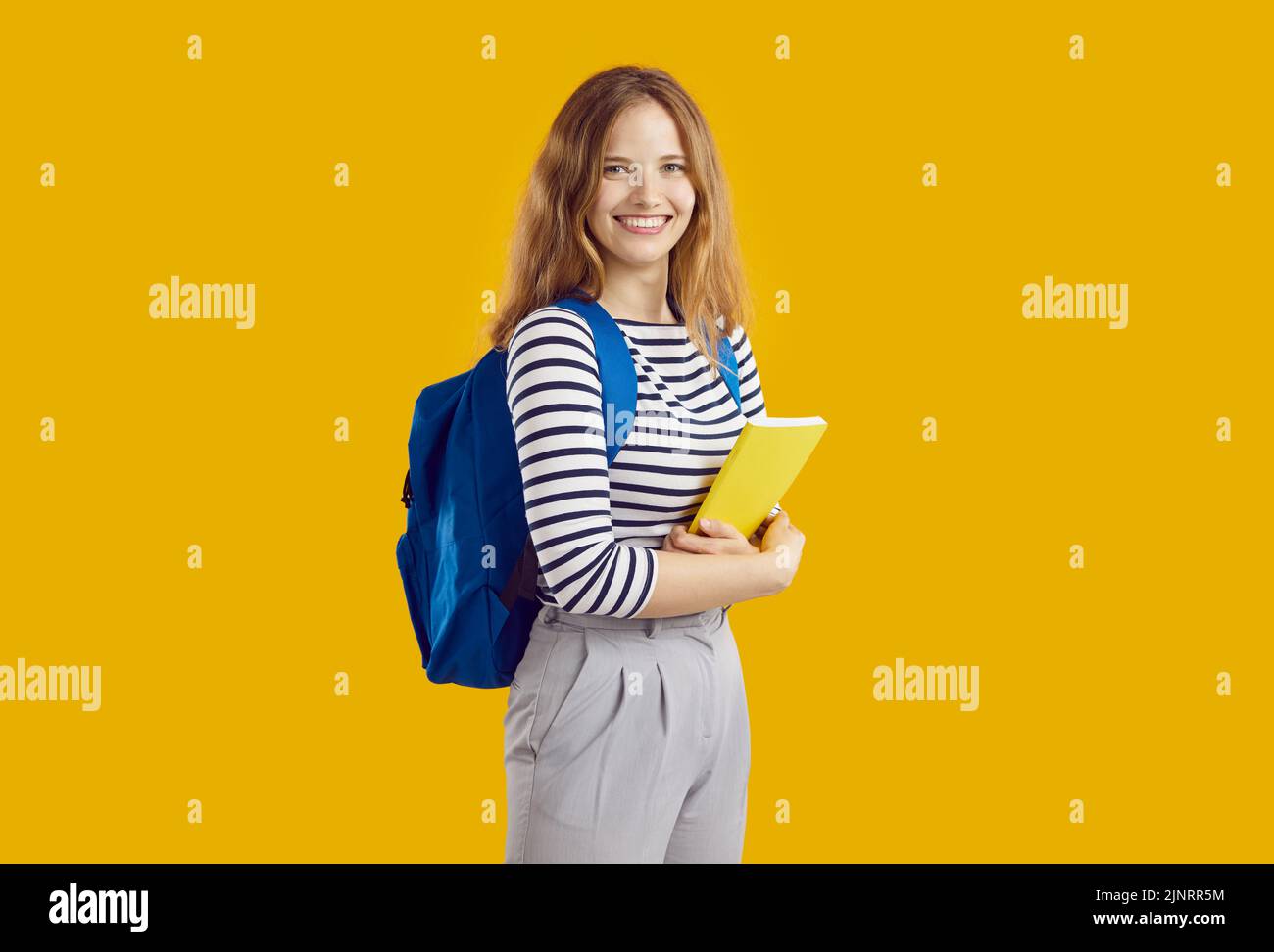 Ritratto di una ragazza allegra con zaino e libro di testo su sfondo arancione. Foto Stock