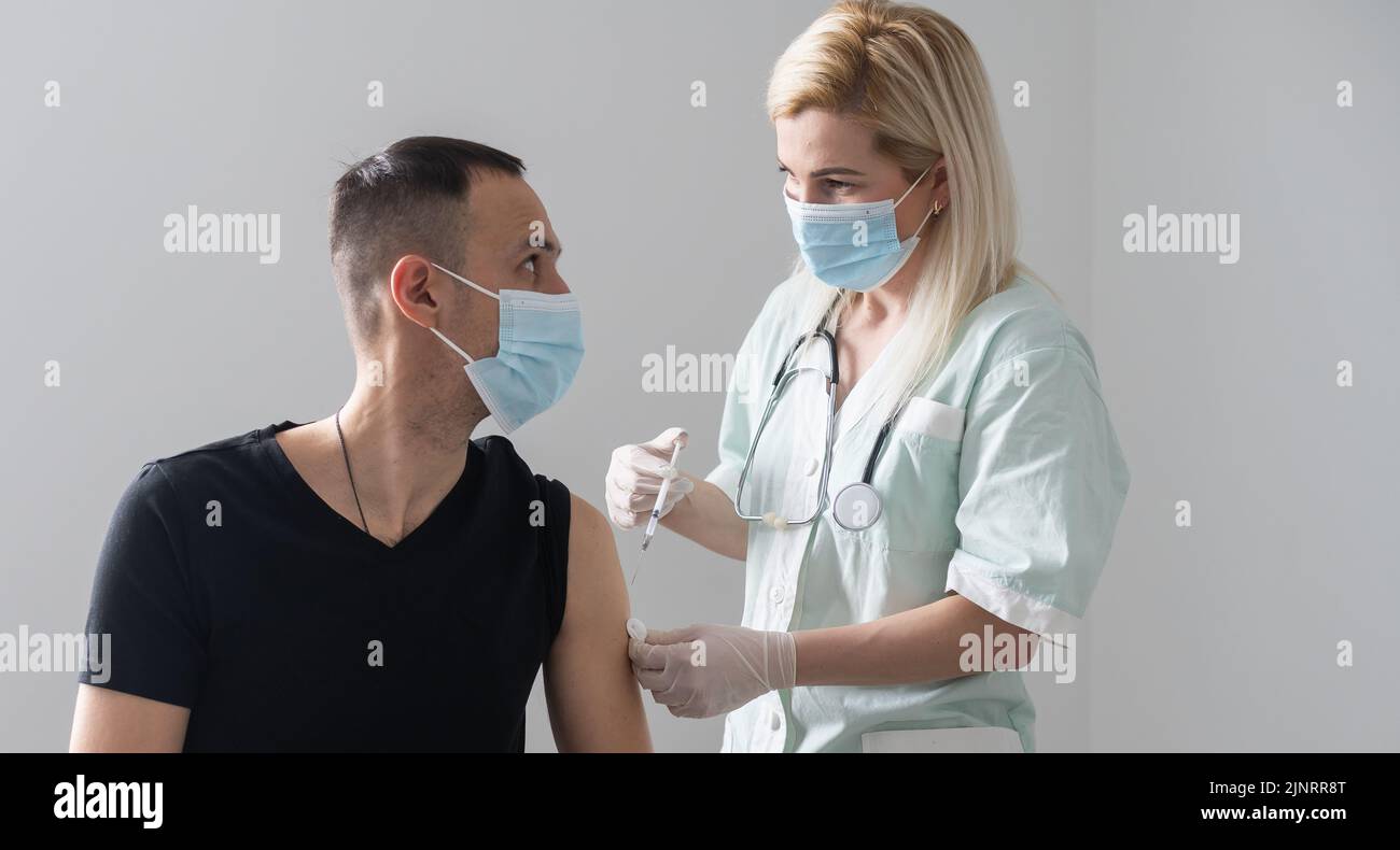 medico donna in una maschera protettiva faccia fa la vaccinazione per l'uomo europeo in ospedale Foto Stock