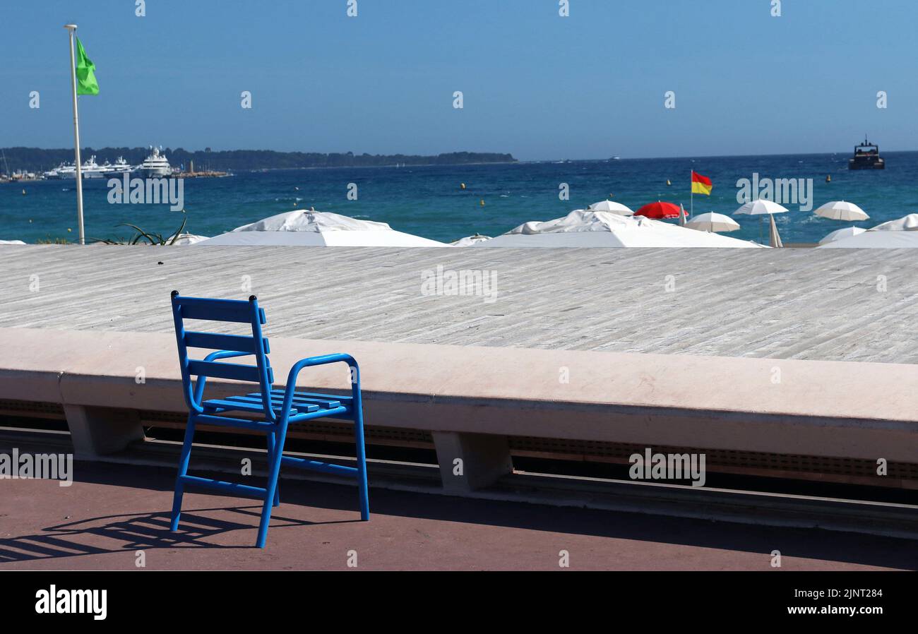 Una delle iconiche sedie blu che fieggiano notoriamente la Promenade de la Croisette, Cannes. Il blu rappresenta il Mediterraneo e il cielo azzurro. Foto Stock