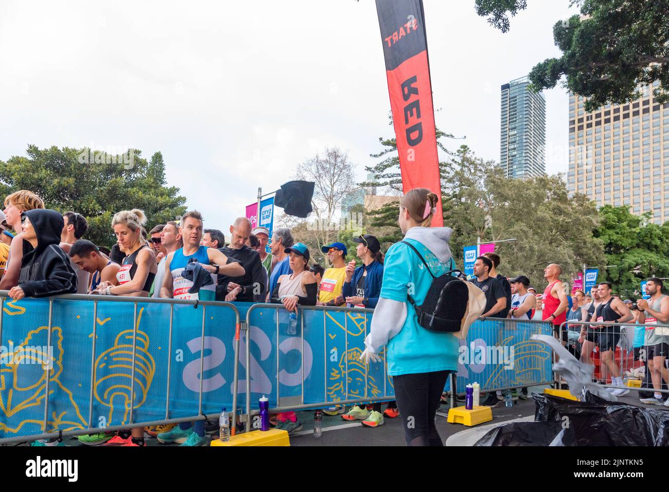 Sydney, Australia, 14 agosto 2022: Oltre 60.000 persone partecipano alla gara del 50th City2Surf a Sydney, la prima dal 2019 dopo le cancellazioni nel 2020 e nel 2021 a causa delle restrizioni del Covid-19. Sullo sfondo di ogni gara ci sono volontari che aiutano l'evento a correre senza intoppi. Nella foto, una ragazza guida attende mentre i vestiti esterni pre-start del corridore scartati volano sopra la barricata verso di lei. L'abbigliamento donato viene successivamente trasferito alle associazioni di beneficenza. Credit: Stephen Dwyer / Alamy Live News Foto Stock