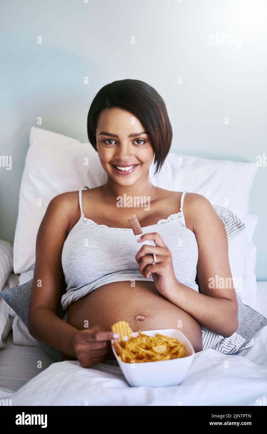 Il bambino mi ha fatto mangiare. Una donna incinta godendo di un cioccolato e patatine fritte a letto. Foto Stock