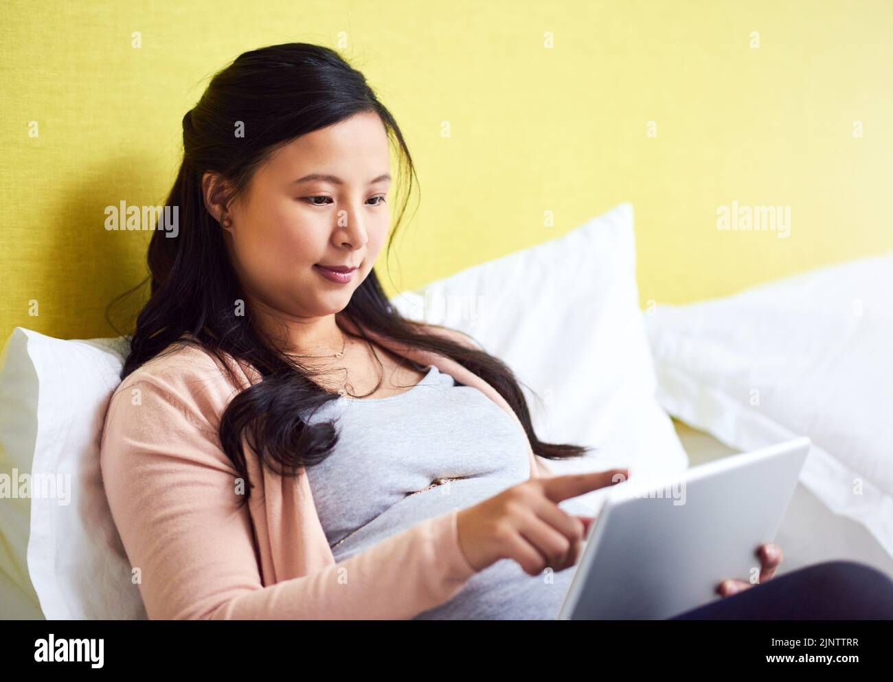 Navigare per tutto il necessario per il suo bambino. Una donna incinta che usa un tablet digitale a casa. Foto Stock